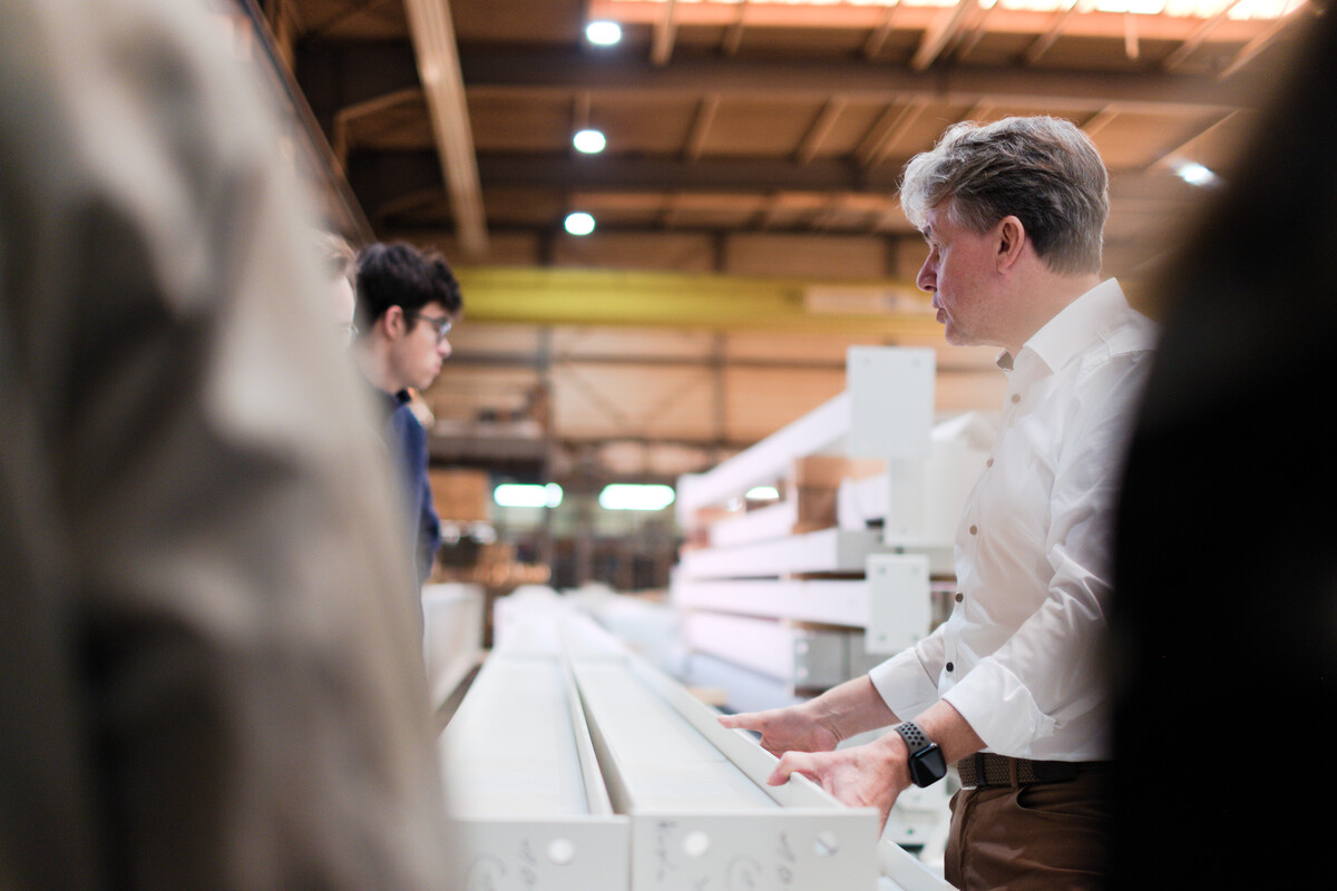 Mitarbeiter in weißem Hemd bedient eine lange Produktions- oder Ladenraumausstellung mit mehreren Regalen.